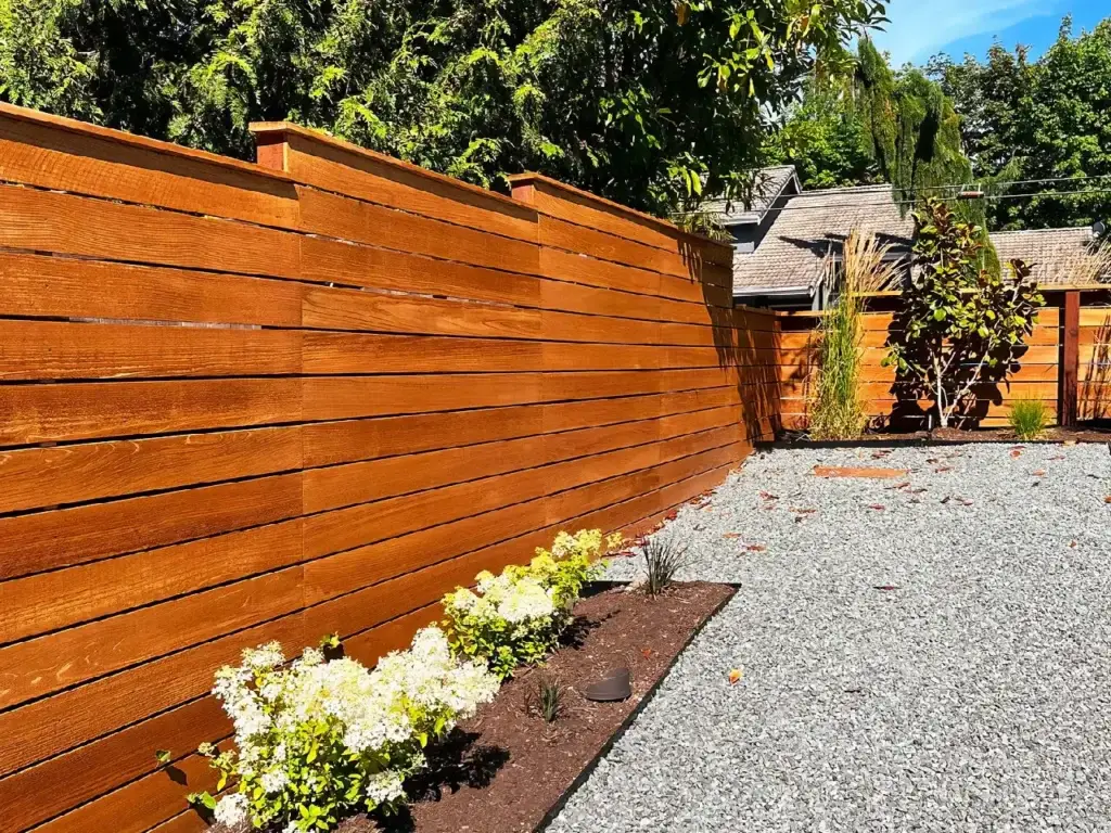 A modern horizontal cedar wood privacy fence with a rich stain providing a secure perimeter for a gravel yard.