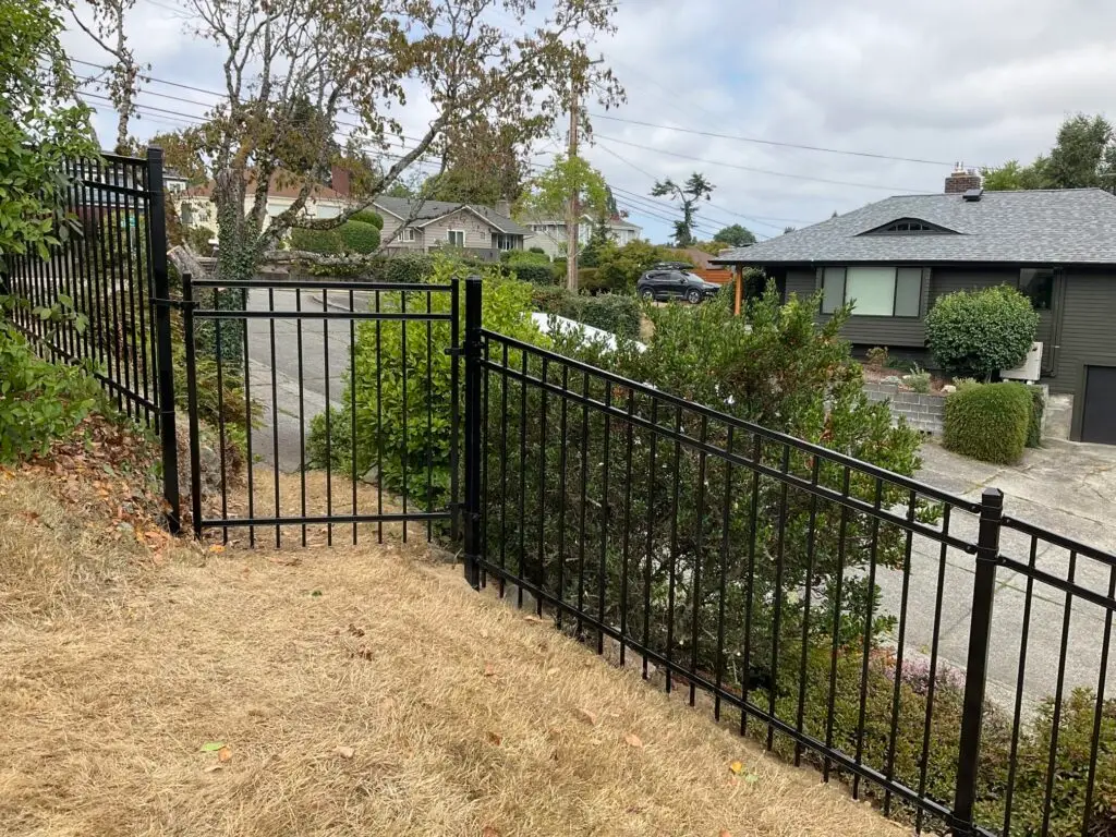 A black ornamental iron picket fence and matching gate installed on a residential hillside to enhance property appearance.