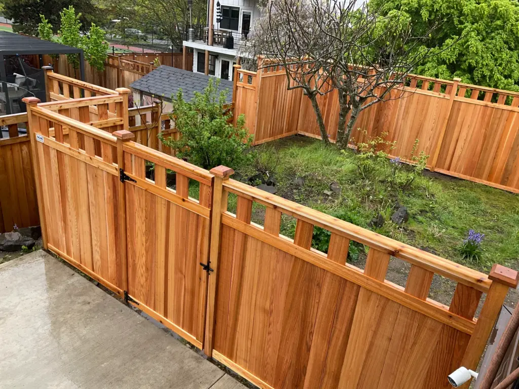 A high-quality cedar fence installation featuring a secure double gate with black hardware and decorative top panels for a finished backyard.
