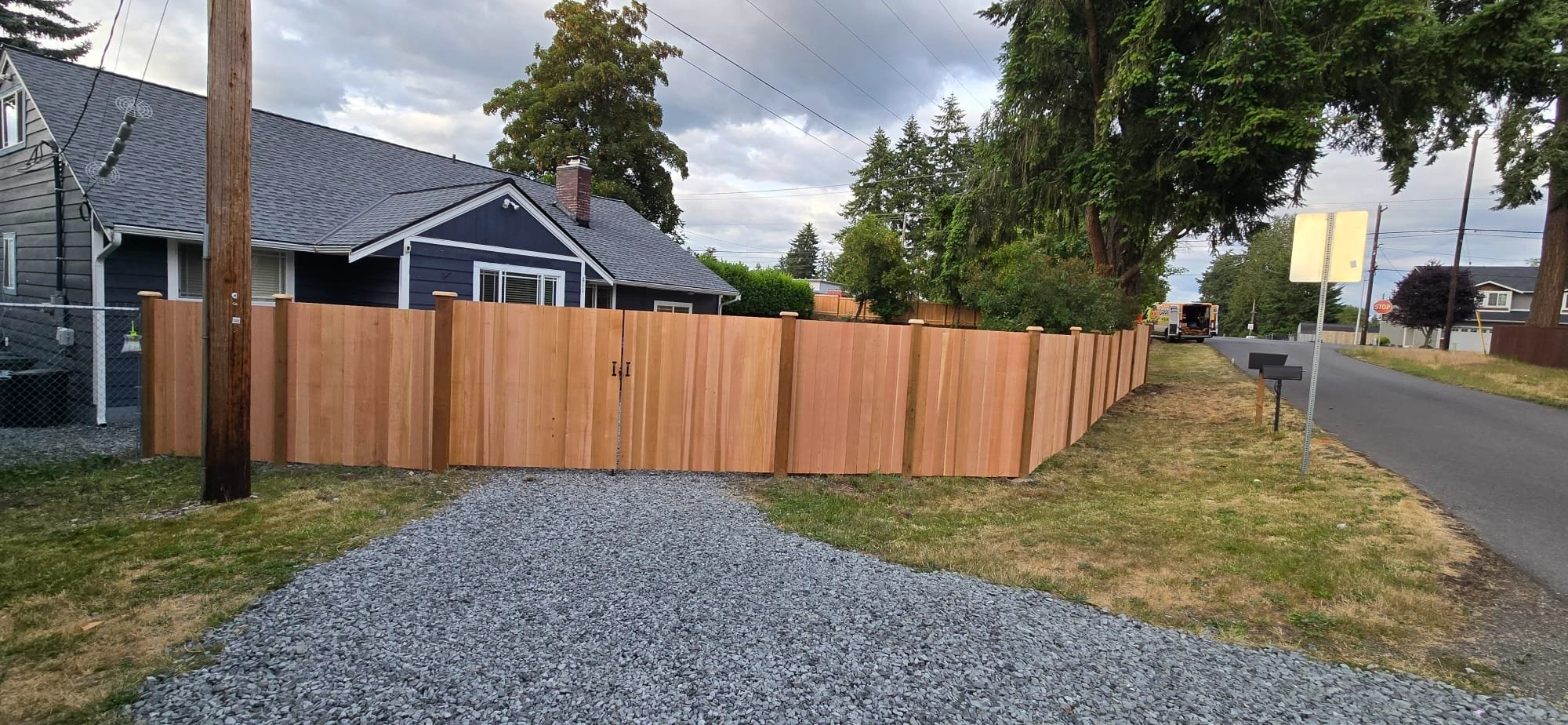 A new Estate Cedar Fence Installation in Spanaway, WA encloses a residential yard next to a gravel driveway.
