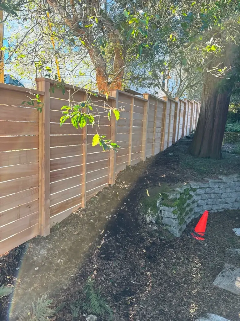 Natural wooden horizontal cedar fence installation in Seattle along a sloped yard with stone landscaping.