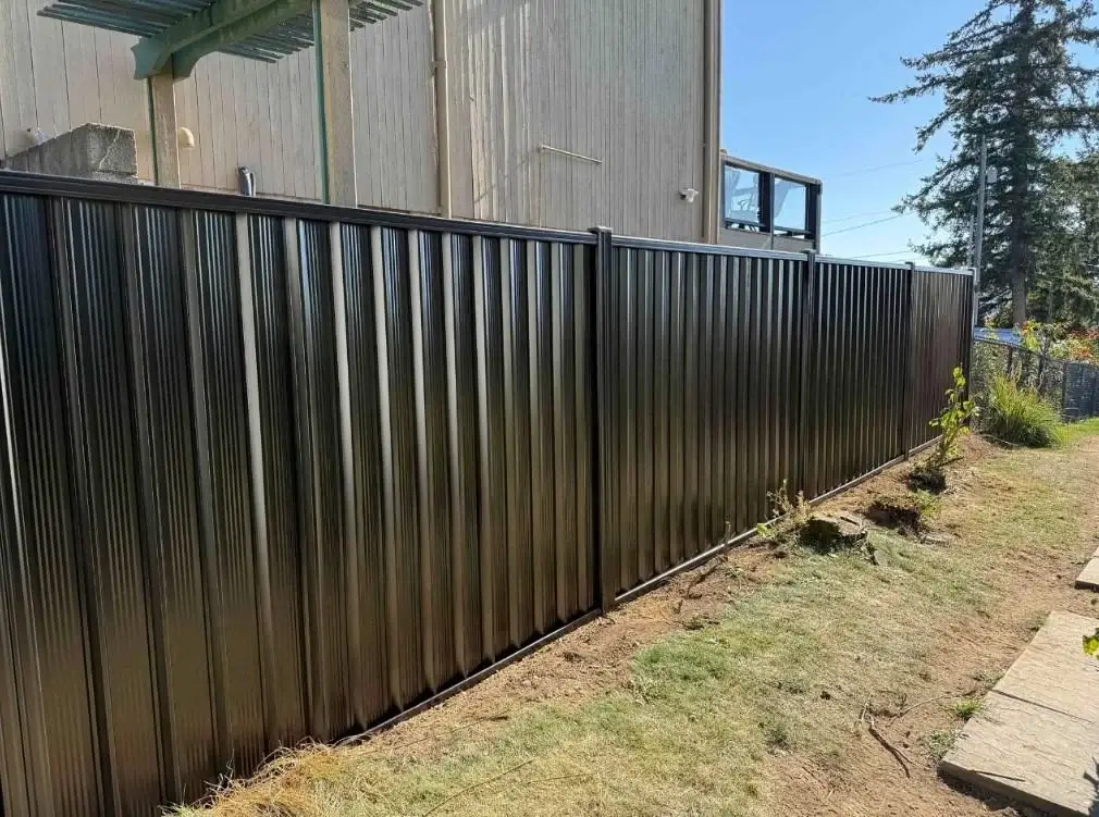 Black ribbed-panel fence with matching posts beside a lawn.